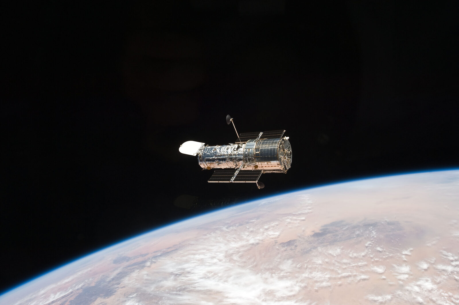 O telescópio espacial Hubble em órbita, fotografado da Terra ao fundo, com os painéis solares abertos.